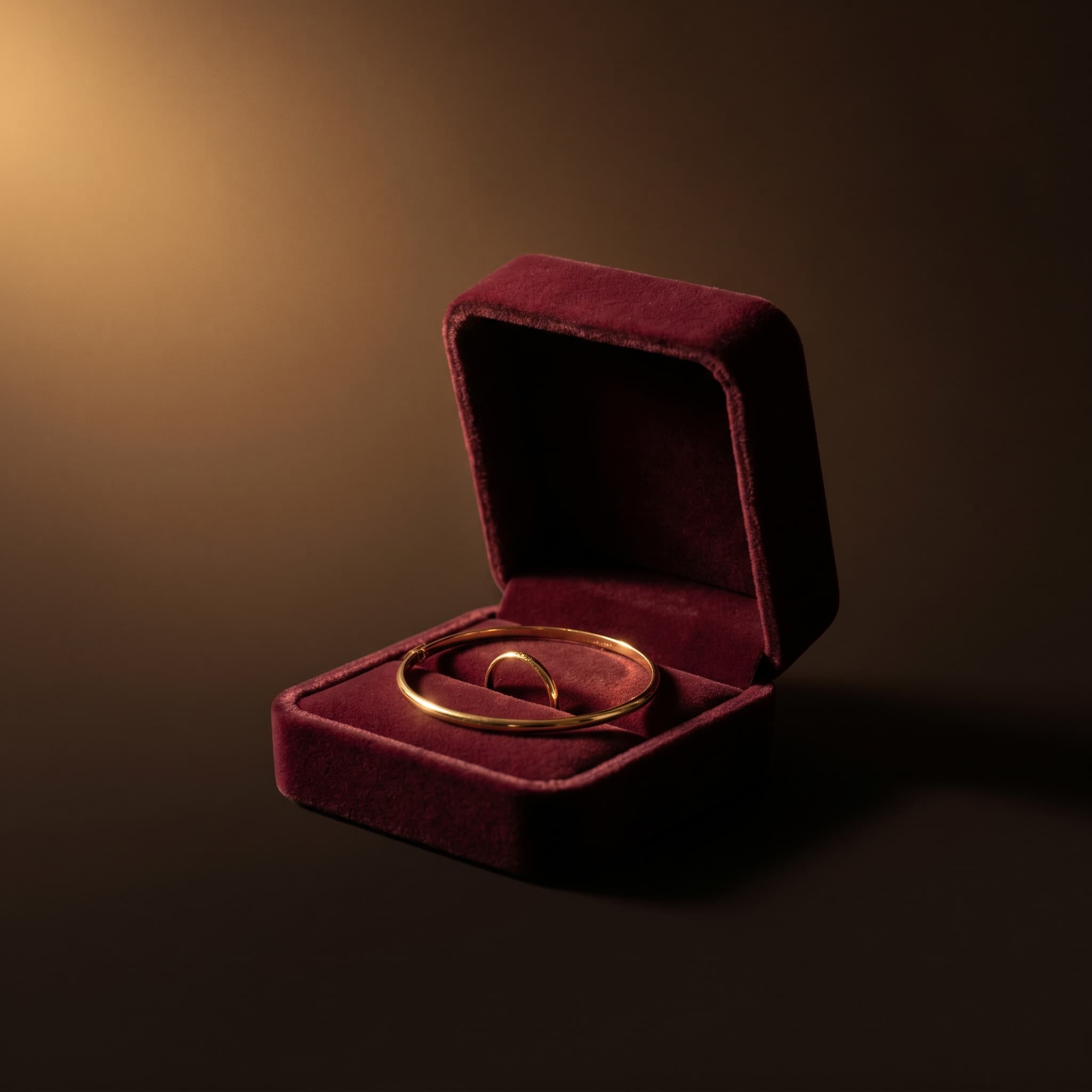 A gold bangle and ring resting in an open burgundy velvet box.